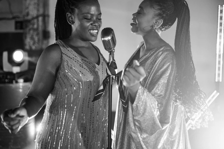 a couple of women standing next to each other holding microphones, an album cover, by Matija Jama, pexels, ebony art deco, live performance, black white, adut akech