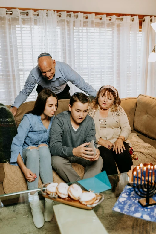 a group of people sitting on a couch in a living room, on a candle holder, looking at his phone, holy ceremony, family photo