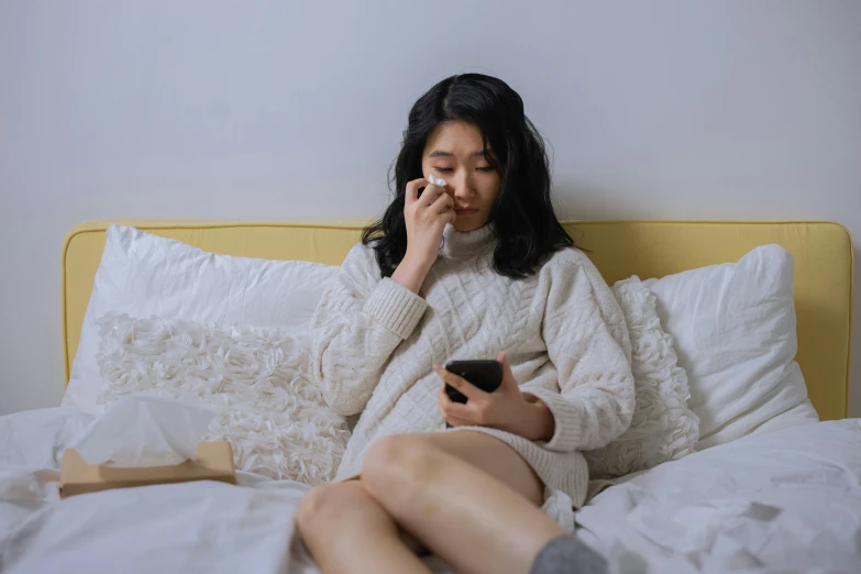 a woman sitting on a bed holding a cell phone, a cartoon, trending on pexels, asian descent, i woke up in pieces, wearing a white sweater, insomnia