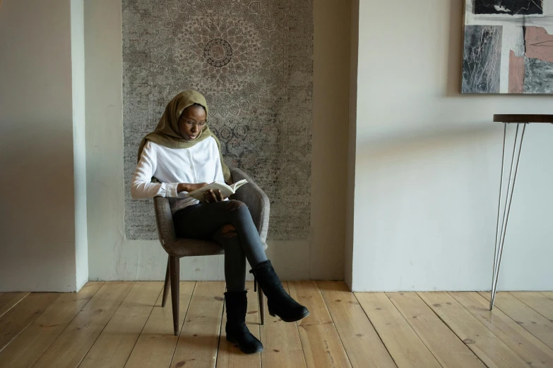 a woman sitting in a chair reading a book, hurufiyya, grey, riyahd cassiem, scandinavian, brown