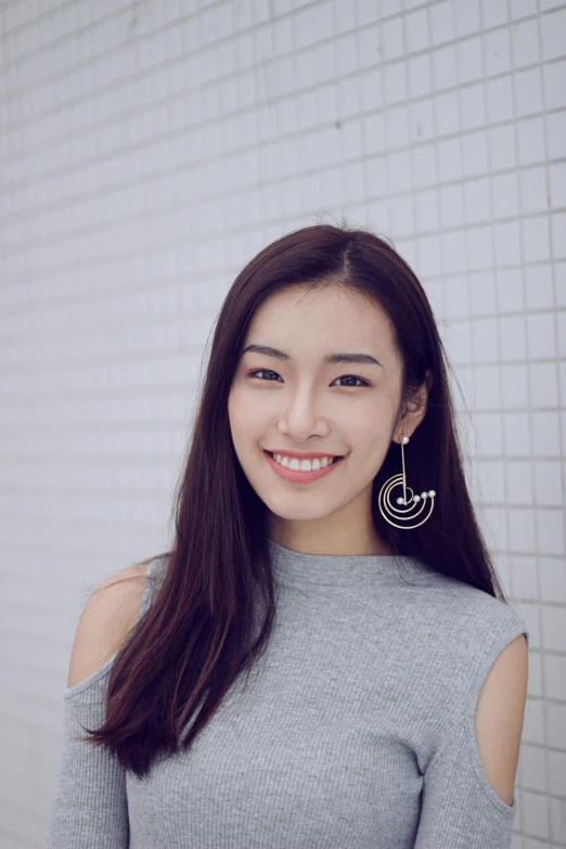 a woman standing in front of a white brick wall, inspired by Kim Jeong-hui, pexels contest winner, shin hanga, 2 d lasercut earrings, smiling young woman, 8 k ), ethnicity : japanese