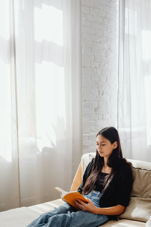 a woman sitting on a couch reading a book, light and space, long black straight hair, promo image, sunlit windows, looking serious