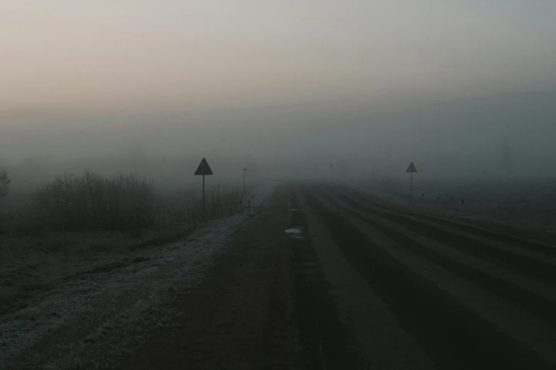 a dirt road in the middle of a foggy field, an album cover, by Attila Meszlenyi, postminimalism, highways, cold winter, low quality photo, early dawn