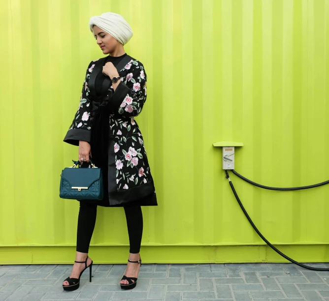 a woman standing in front of a green wall, inspired by Maryam Hashemi, hurufiyya, wearing black coat, floral couture, monochrome, engineer