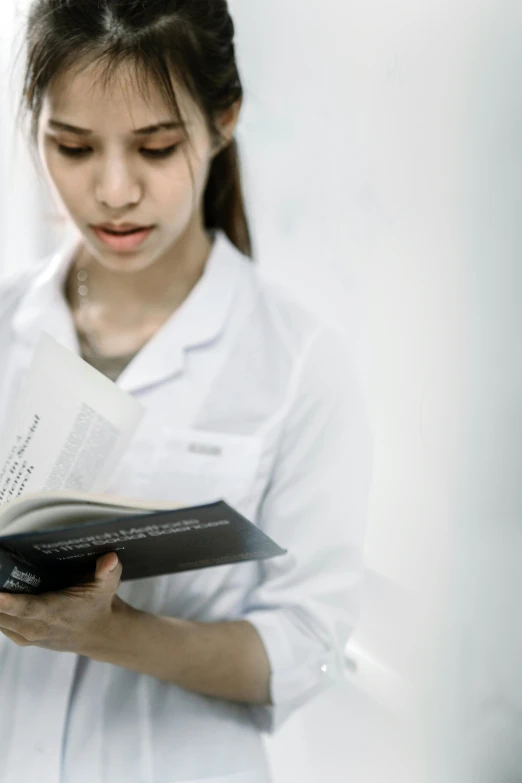 a woman in a white shirt is reading a book, wearing a lab coat, high-quality photo, stockphoto, girl wearing uniform