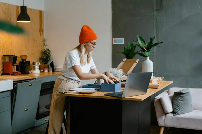 a woman sitting at a table working on a laptop, by Julia Pishtar, trending on pexels, arbeitsrat für kunst, with black beanie on head, delivering parsel box, thumbnail, casey cooke