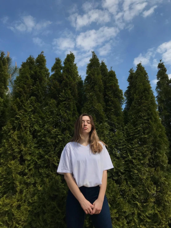 a man standing in front of a row of trees, an album cover, by Carey Morris, unsplash contest winner, portrait sophie mudd, white t-shirt, 🌲🌌, uniform off - white sky