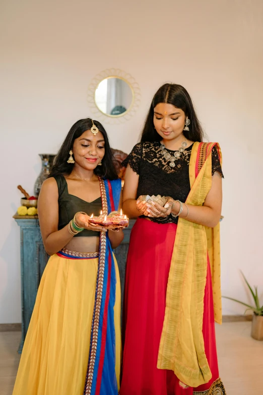 a couple of women standing next to each other, colorful adornments, candles, jayison devadas, gen z