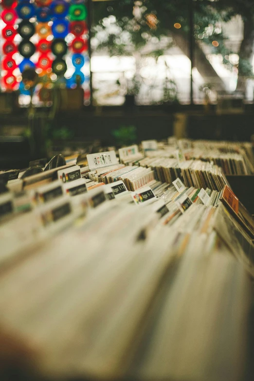 a bunch of records sitting on top of a table, trending on unsplash, shelves filled with tomes, defocused bars in the foreground, marketplace, low fi