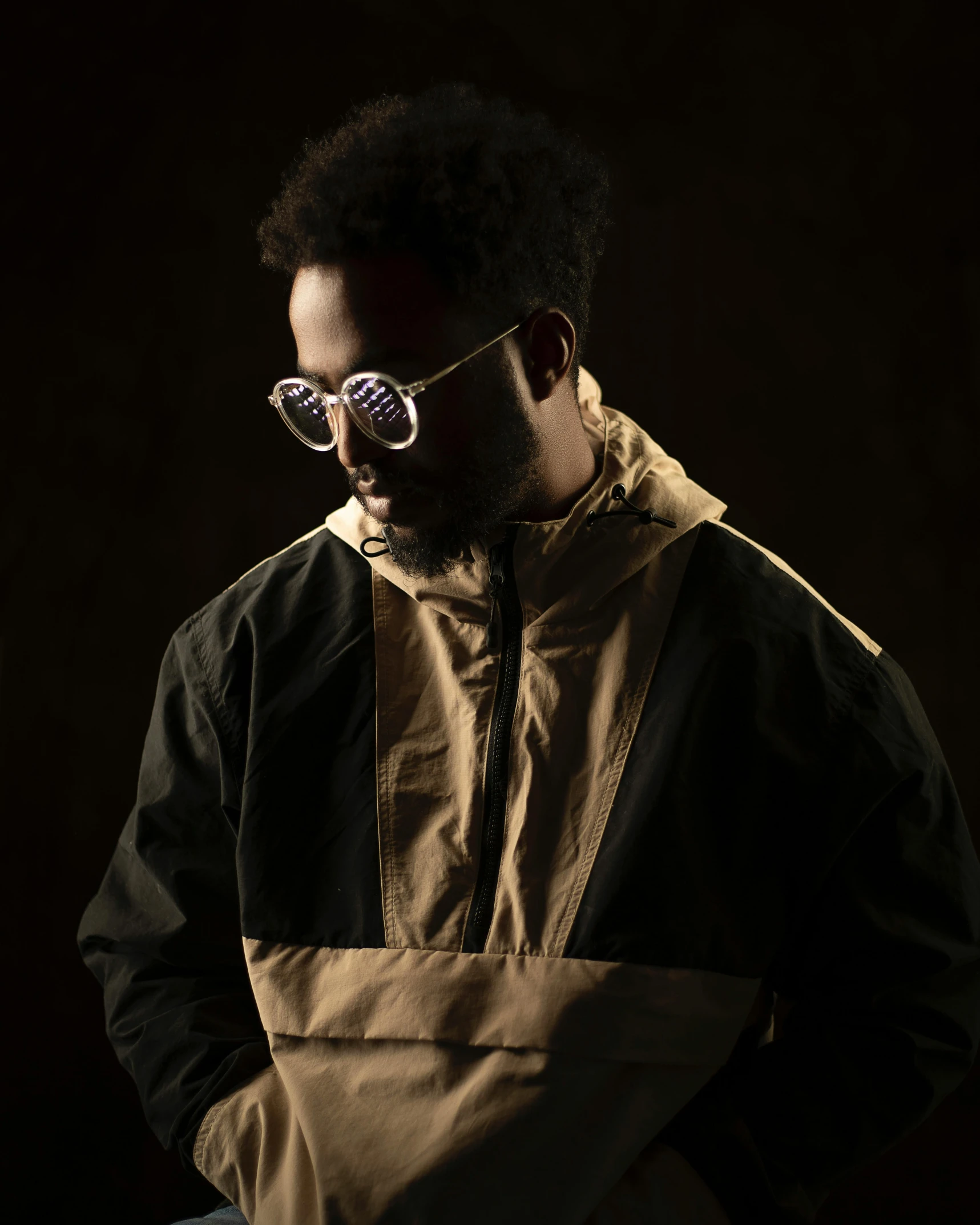 a man in a brown and black jacket and sunglasses, inspired by Afewerk Tekle, unsplash, afrofuturism, dark studio light, wearing a track suit, reflective puffy coat, wearing black rimmed glasses