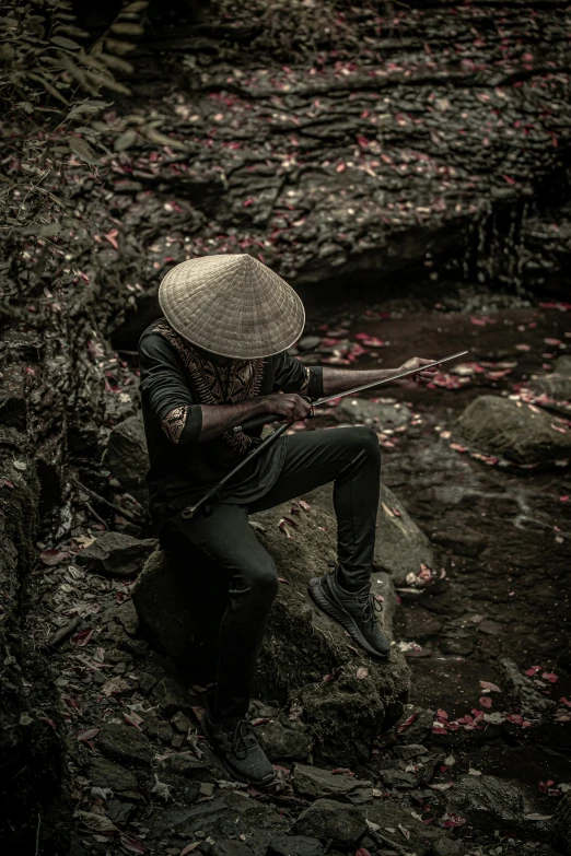 a man sitting on a rock with a rifle, an album cover, inspired by Kanō Hōgai, pexels contest winner, sumatraism, dark hat, vietnam, actor, 2019 trending photo