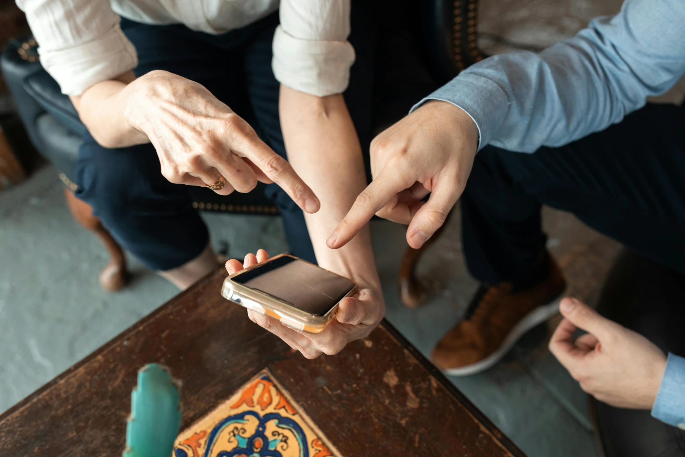 a group of people sitting around a table looking at a cell phone, by Matthias Stom, trending on pexels, interactive art, background image, hands with five fingers, family photo