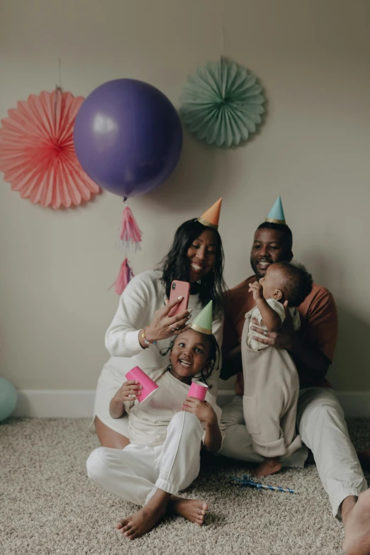 a group of people sitting next to each other on the floor, a polaroid photo, pexels, happening, party hats, husband wife and son, black people, holding a balloon