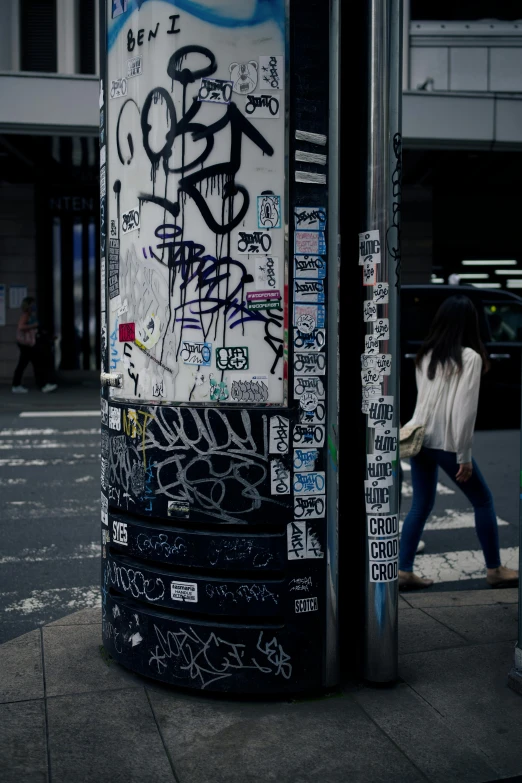 a woman walking past a bus stop covered in graffiti, trending on unsplash, stickers, low quality photo, japanese downtown, close-up shot taken from behind