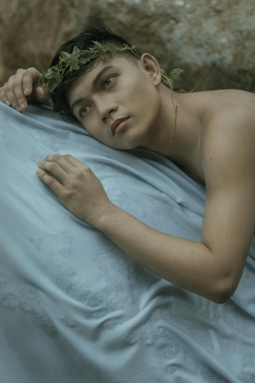 a man laying on top of a bed covered in blue sheets, an album cover, by Basuki Abdullah, pexels contest winner, delicate androgynous prince, portrait of a dryad, ignant, john jude palencar