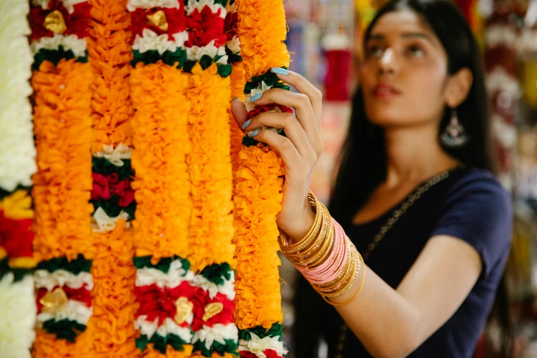 a woman standing in front of a wall of flowers, trending on unsplash, hurufiyya, hindu ornaments, ribbons and flowers, profile image, with yellow cloths