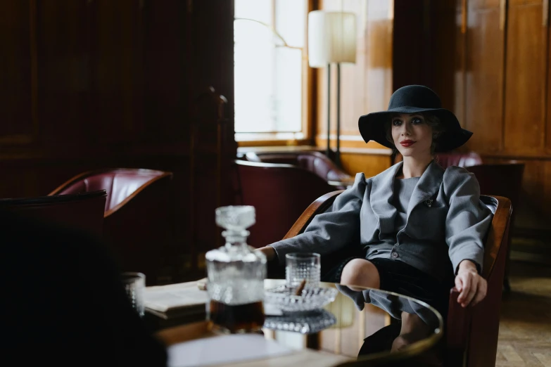 a woman sitting in a chair with a hat on, unsplash, costumes from peaky blinders, sitting at the parlament meeting, silk spectre, on a coffee table