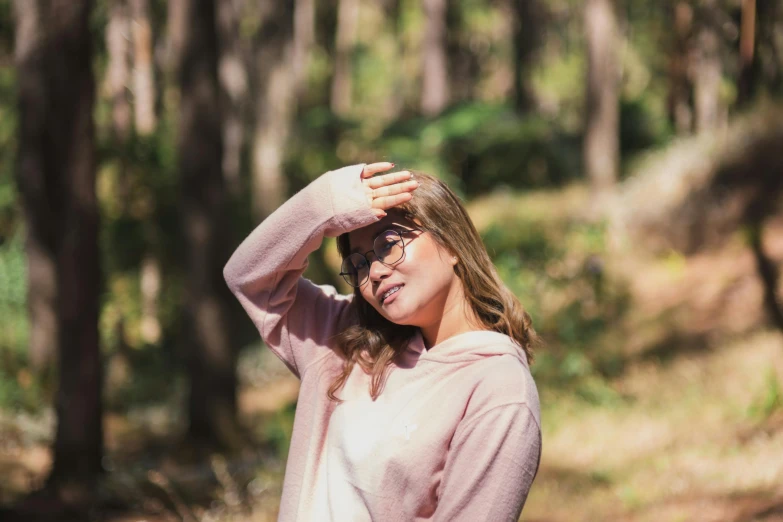 a woman standing in the woods with her hands on her head, pexels contest winner, pink glasses, in avila pinewood, avatar image, wearing casual sweater
