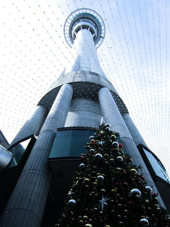 a tall christmas tree in front of a tall building, inspired by Zha Shibiao, hurufiyya, auckland sky tower, view from ground, spacious, naboo