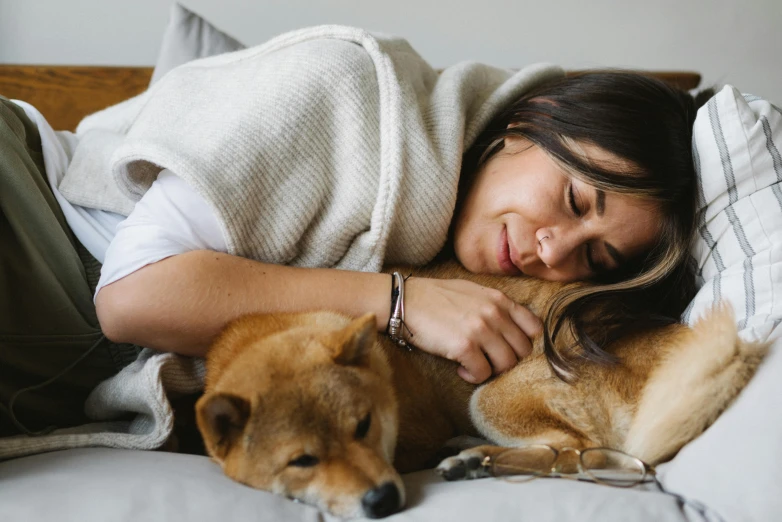 a woman laying on top of a bed next to a dog, trending on pexels, cuddling her gremlings, manuka, acupuncture treatment, hugging each other