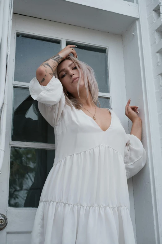 a woman in a white dress leaning against a door, inspired by Elsa Bleda, pexels contest winner, wearing white v - neck top, flowy hair, witchy clothing, woman in streetwear