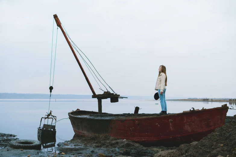 a woman standing on top of a boat on a beach, an album cover, by Emma Andijewska, pexels contest winner, film movie still, fishing boat, saoirse ronan, shipwreck