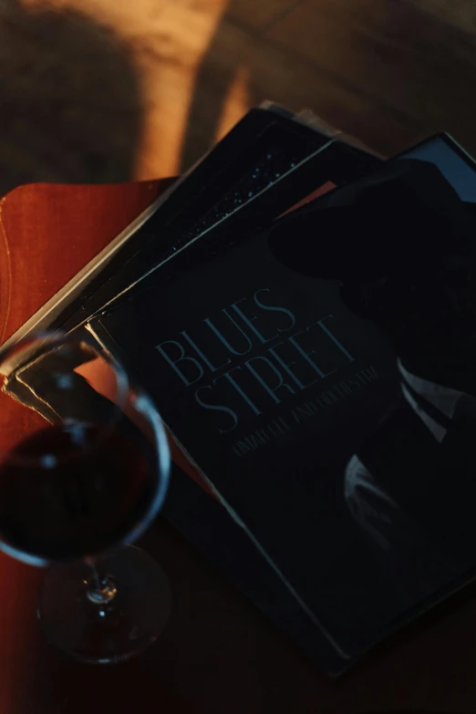 a book sitting on top of a table next to a glass of wine, an album cover, inspired by Louis Stettner, dark street, blues, thumbnail, moviestill