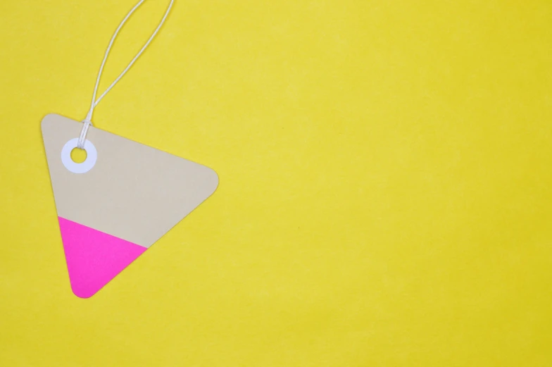 a tag hanging from a string on a yellow background, inspired by Frederick Hammersley, trending on pexels, neon pink, flat triangles, holiday, presents
