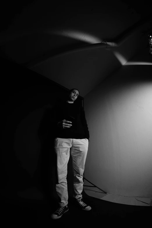 a black and white photo of a man standing in front of a light, by Leo Leuppi, yung lean, in a basement, ((portrait)), adam varga