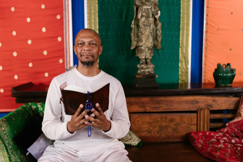 a man sitting on a couch reading a book, a portrait, by Dan Content, pexels, renaissance, standing in a buddhist temple, nubian, full frame image, holding a holy symbol