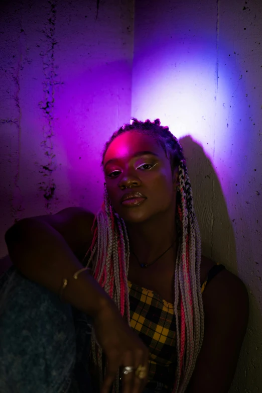 a woman with dreadlocks sitting against a wall, an album cover, trending on pexels, afrofuturism, colored lights, bisexual lighting, ( ( dark skin ) ), iridescent image lighting