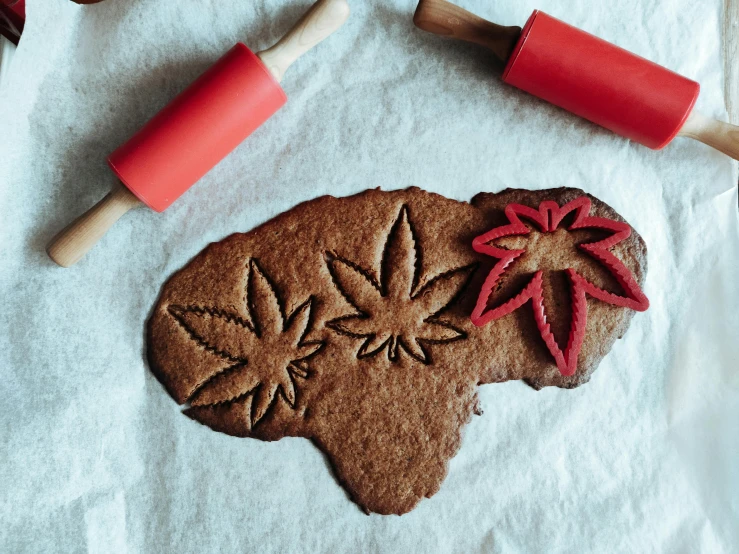 a cookie sitting on top of a table next to a rolling pin, inspired by Mary Jane Begin, trending on pexels, art nouveau, marijuana plants, paper cut out, red leaves, made of bronze