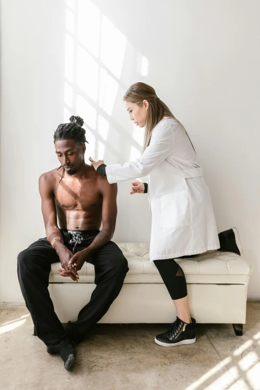 a man sitting on top of a couch next to a woman, by Washington Allston, pexels contest winner, renaissance, with a stethoscope, man is with black skin, muscle tissue, on a white table