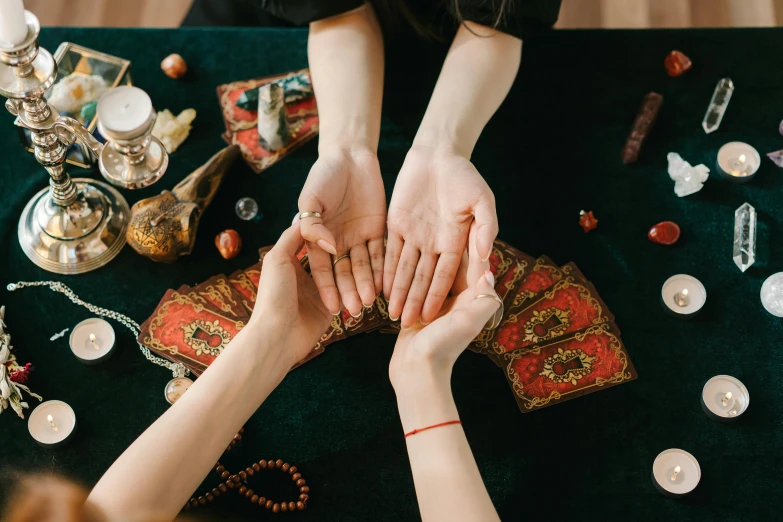 a group of people holding hands over a table, a photo, by Julia Pishtar, trending on pexels, renaissance, tarot design, apothecary, fan favorite, thumbnail