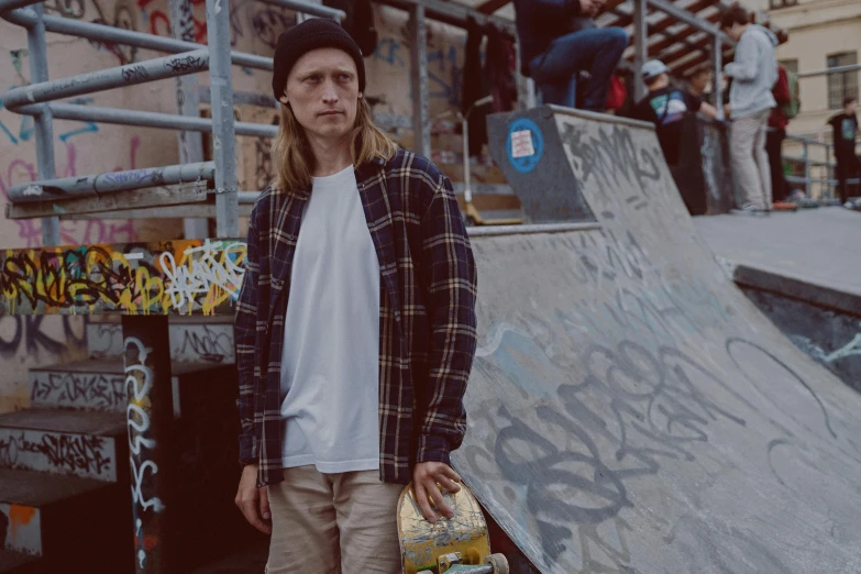 a man standing in front of a skateboard ramp, a picture, inspired by Seb McKinnon, wearing a flannel shirt, federation clothing, lane brown, stood in a tunnel