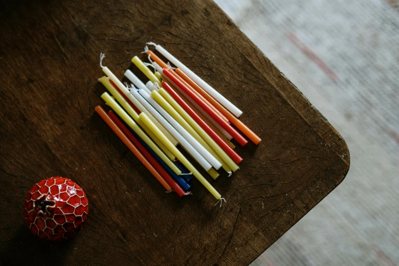 a pile of candles sitting on top of a wooden table, unsplash, process art, with a straw, primary colors, orange and white, tiny sticks