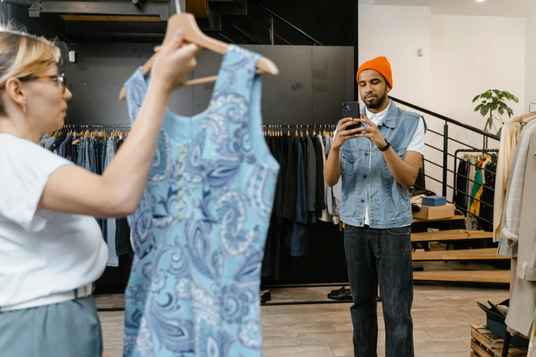 a man standing next to a woman in a clothing store, a photo, by Everett Warner, pexels contest winner, checking her phone, wearing a blue dress, antoine-jean gr, patterned clothing