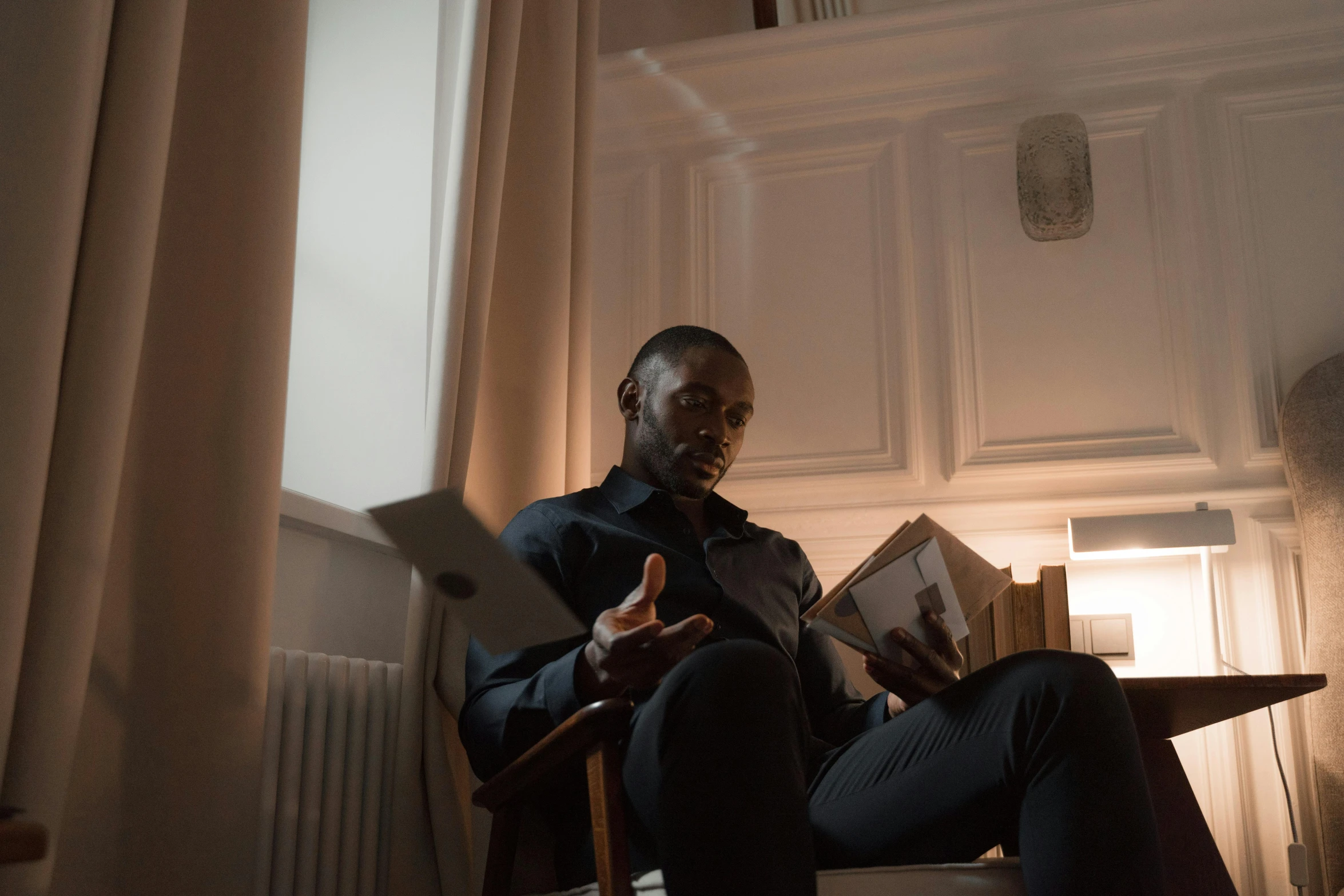 a man sitting in a chair reading a book, a portrait, pexels contest winner, ( ( dark skin ) ), black, **cinematic, sitting in french apartment