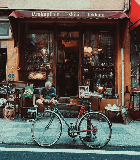 a man sitting on a bench in front of a store, pexels contest winner, bicycle in background, istanbul, an escape room in a small, vintage old