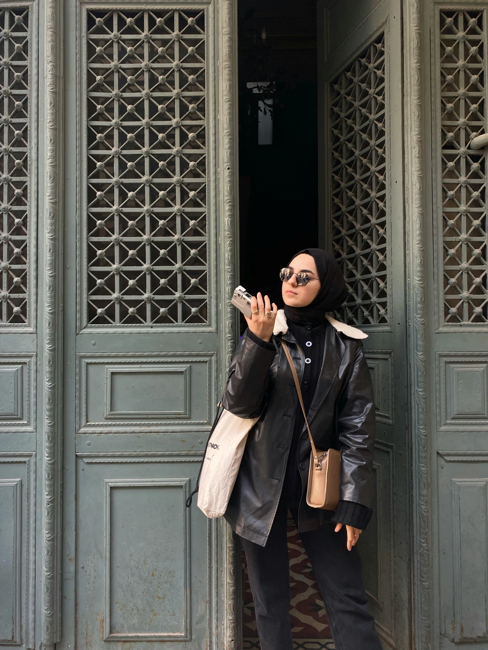 a woman standing in the doorway of a building, a picture, inspired by Maryam Hashemi, trending on unsplash, wearing a full leather outfit, selfie shot straight on angle, cairo, ☁🌪🌙👩🏾