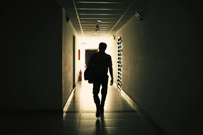 a silhouette of a person walking down a hallway, pexels, happening, he is at college, somber lighting, schools, light over boy