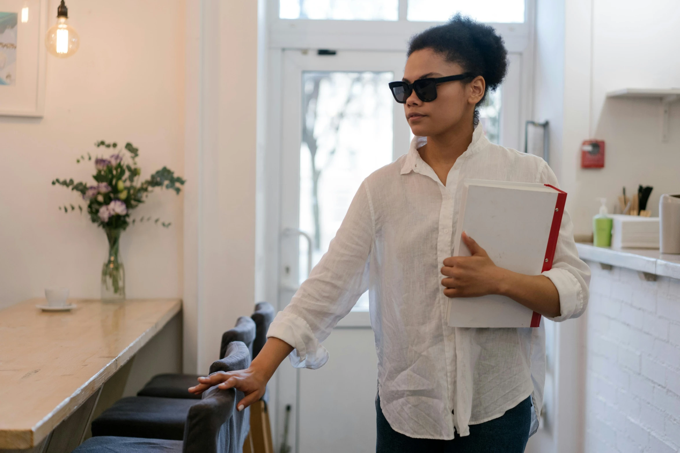 a woman standing in a kitchen holding a book, by Carey Morris, pexels contest winner, visual art, wearing shades, walking to work, tessa thompson, wearing a white button up shirt