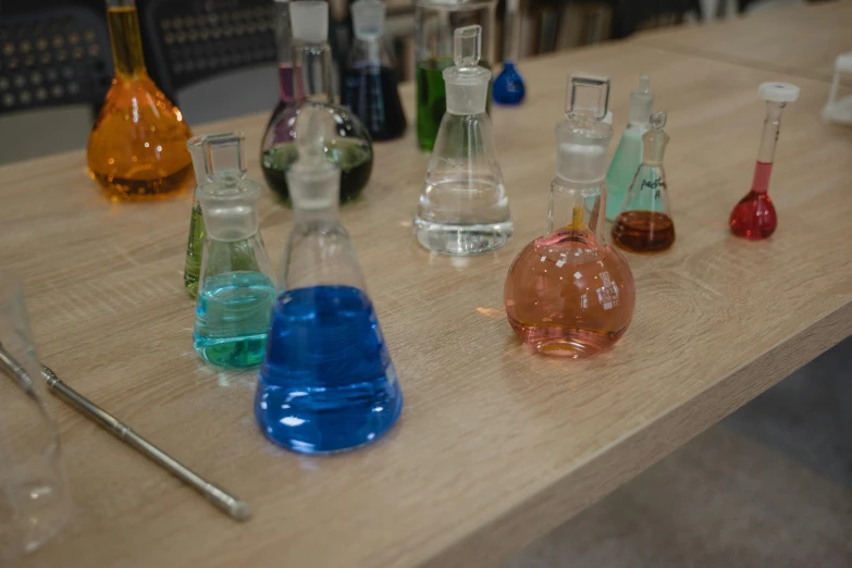 a wooden table topped with lots of different colored liquids, unsplash, inside a science facility, fan favorite, flasks, educational