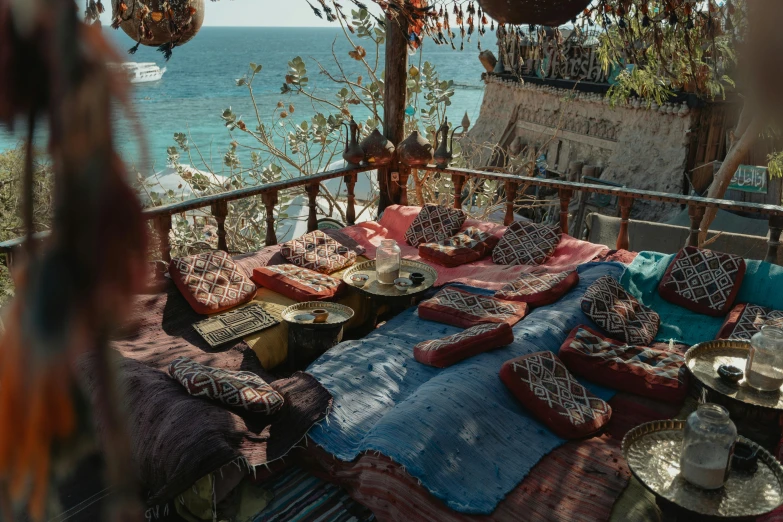 a bed sitting on top of a wooden floor next to the ocean, middle eastern style vendors, on a cliff, vintage aesthetic, lounge background