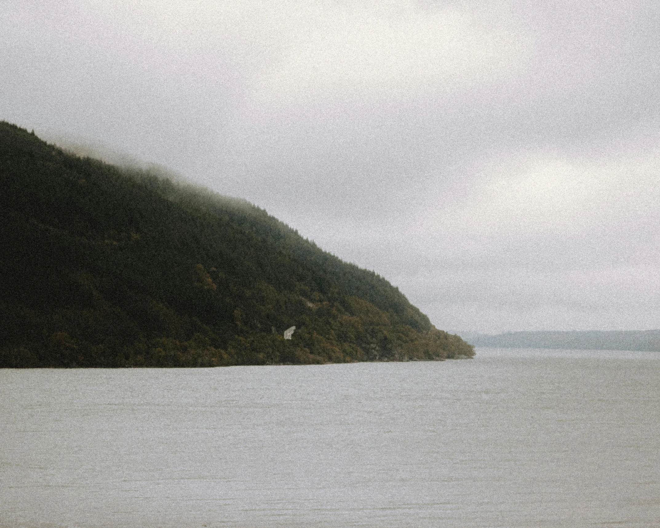 a boat in the middle of a large body of water, pexels contest winner, hudson river school, overcast gray skies, hill with trees, grainy footage, an eerie