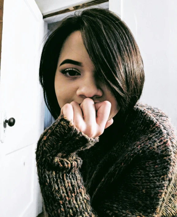 a woman leaning against a wall with her hand on her chin, inspired by Dulah Marie Evans, trending on instagram, with a bob cut, wearing a sweater, teenage vanessa morgan, weathered olive skin
