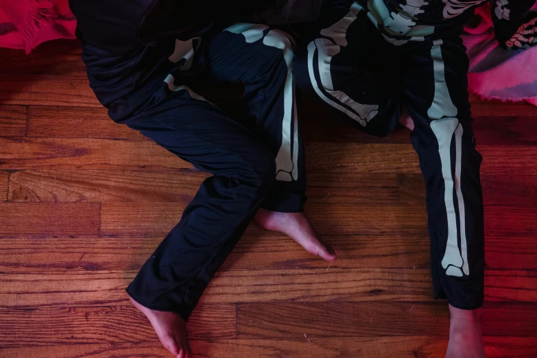 a couple of people sitting on top of a wooden floor, by Nina Hamnett, unsplash, massurrealism, skeleton corpse, wearing a track suit, close-up on legs, halloween