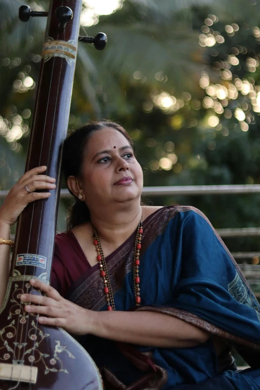 a woman sitting on a bench playing a musical instrument, by Sunil Das, double bass, ritu kumar, profile image, portrait image