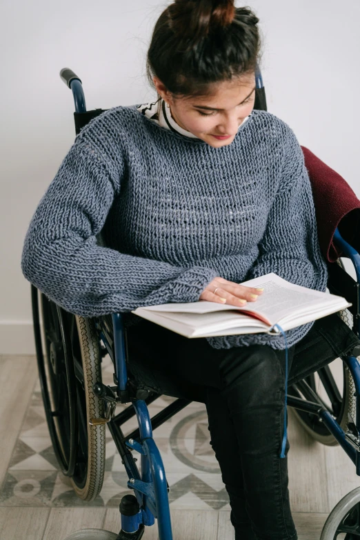 a woman in a wheelchair reading a book, wearing a sweater, high details, edited, wholesome