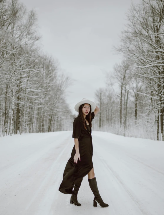 a woman walking across a snow covered road, by Andrew Stevovich, pexels contest winner, wearing black dress and hat, wears brown boots, in white room, jackie tsai style